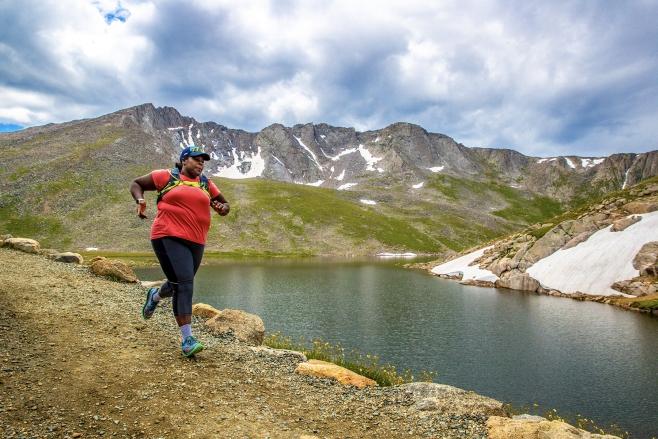 Mirna Valerio running along a lake with mountains in the distance
