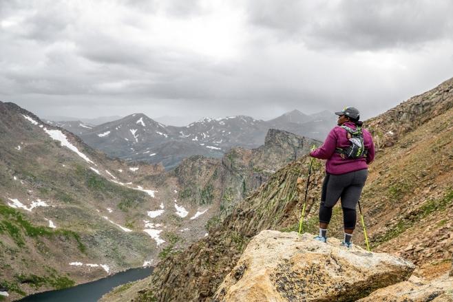 Mirna Valerio holding walking sticks and standing on a mountain